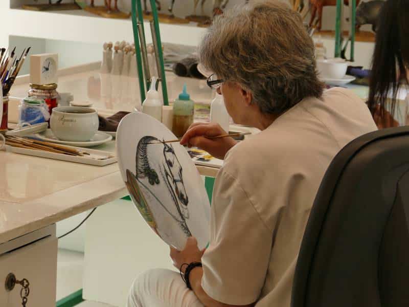 femme au Portugal en train de peindre un motif de cheval sur une assiette en porcelaine, publiée dans les boomeuses